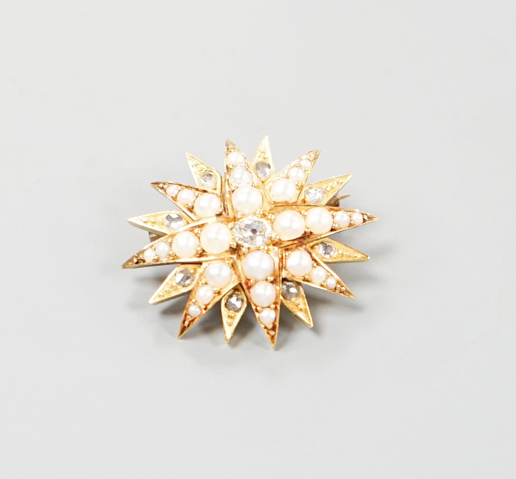 An Edwardian yellow metal, graduated split pearl and single stone diamond set starburst brooch(adapted?), 24mm, gross weight 6.5 grams.